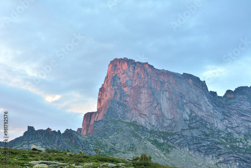 A high rock with a steep steep slope is painted orange by the setting sun on a warm summer evening.