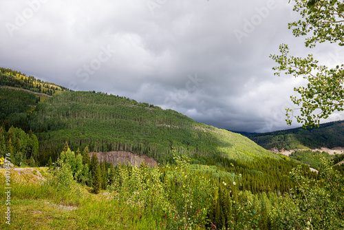 Photograph of mountain and hills filled with overgrowth greenery foliage and woodlands stormy rain clouds.