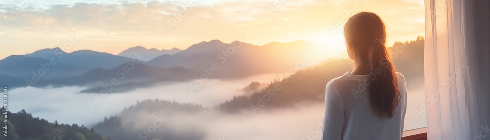 A person gazing at a tranquil sunrise over misty mountains from a window, evoking peace and serenity in the natural landscape.