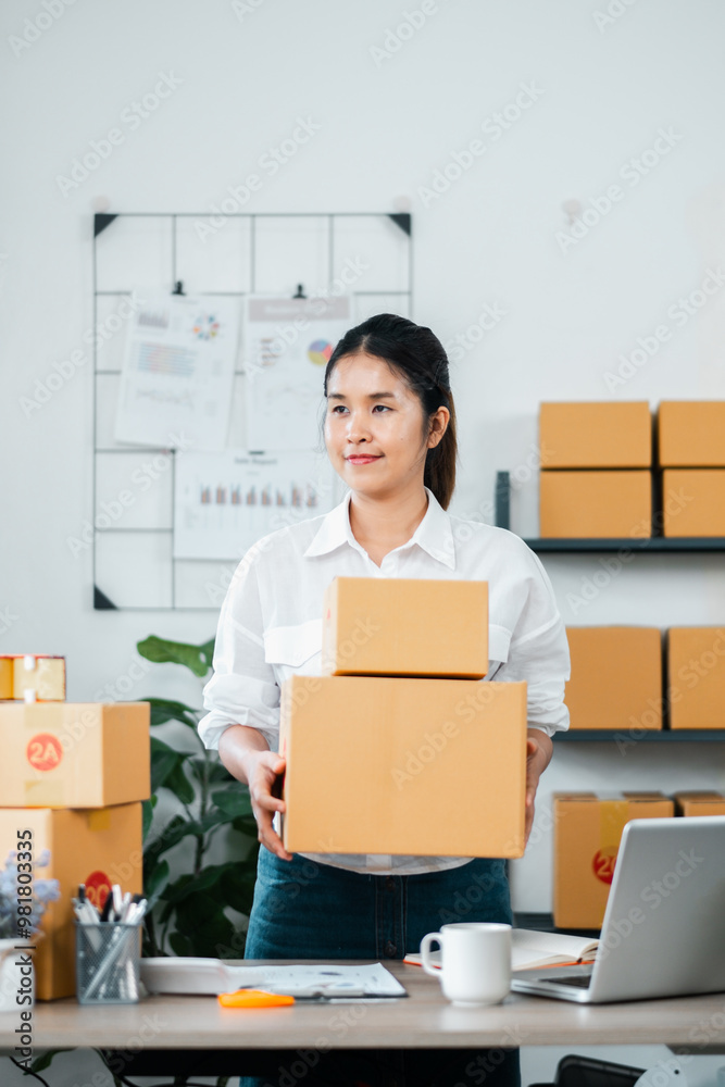 Young woman entrepreneur holding cardboard boxes in a modern office setting, surrounded by shelves and a laptop. Young woman entrepreneur holding cardboard boxes in a modern office setting, surrounded by shelves and a laptop.