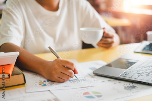 A business professional working on financial reports with a laptop and coffee, highlighting productivity and modern office environment.