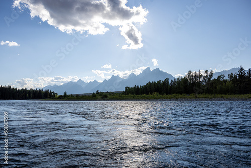 Wide landscape photograph calm rippling surface of the snake river in the grand Tetons national park, Wyoming. Dramatic clouds, bright blue sky and Teton Mountains in the horizon.