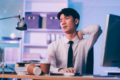 Young pensive asian man working late concentrated and serious in front of computer at night in dark office, Late night working or studying concept.