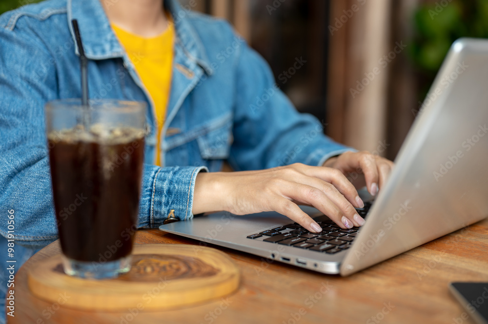 A close-up of a woman working on her laptop in a coffee shop, typing on the laptop keyboard. A close-up of a woman working on her laptop in a coffee shop, typing on the laptop keyboard.