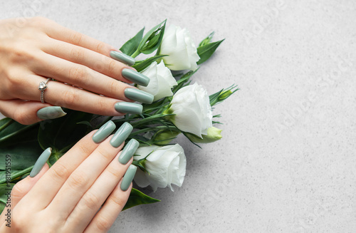 Elegant hands with green nail polish holding a bouquet of white roses on a light gray surface in a stylish arrangement photo