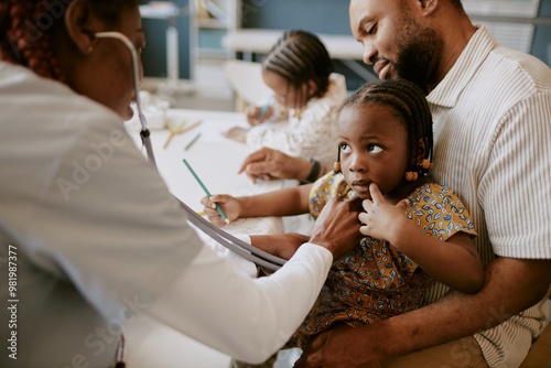 Fotografie Child sitting on fathers lap holding his hand while doctor examining her