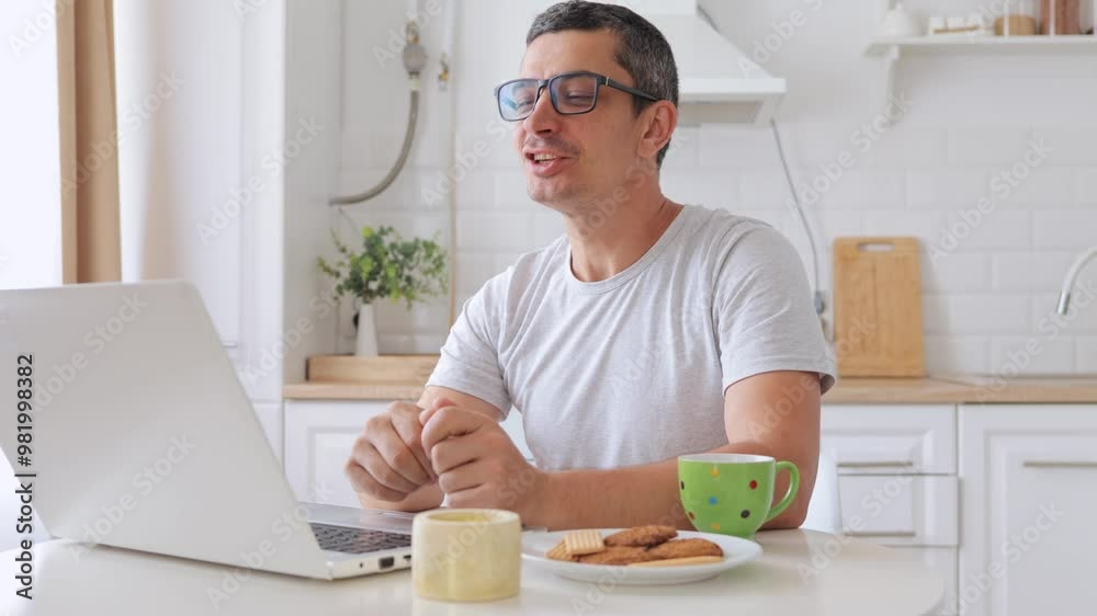 Delighted man freelancer using laptop for online communication waving hi on video call via portable computer working from home on notebook browsing web doing remote work in kitchen Delighted man freelancer using laptop for online communication waving hi on video call via portable computer working from home on notebook browsing web doing remote work in kitchen