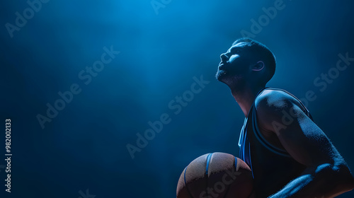 Basketball Player Holding Ball in Dramatic Blue Lighting on blue background