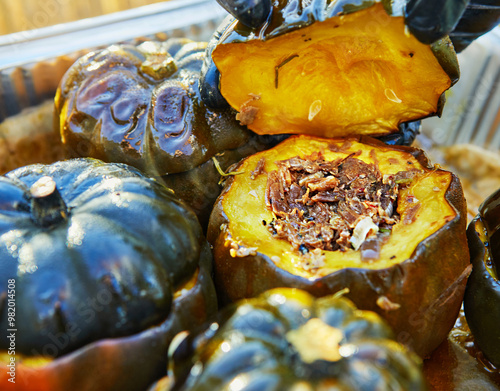 Close-up of a gloved hand holding open a roasted squash stuffed with shredded beef, garlic, and red pepper, ready to be served photo