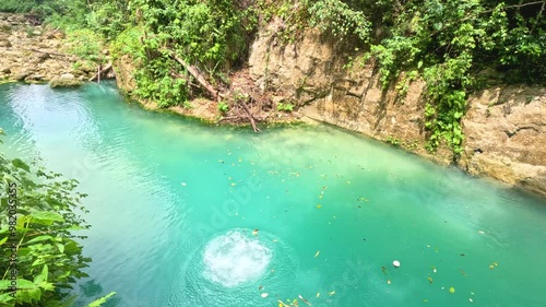 A man umps from a 10meter platform while canyoneering at Kawasan Falls in Cebu, Philippines. She runs and jumps from the platform down into the bright blue water below.