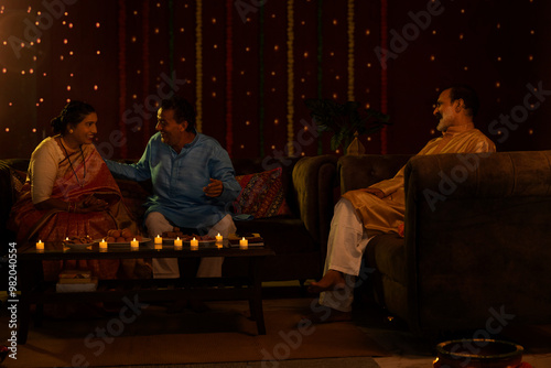 Senior couple sitting on sofa with friend at home and talking during Diwali celebration photo