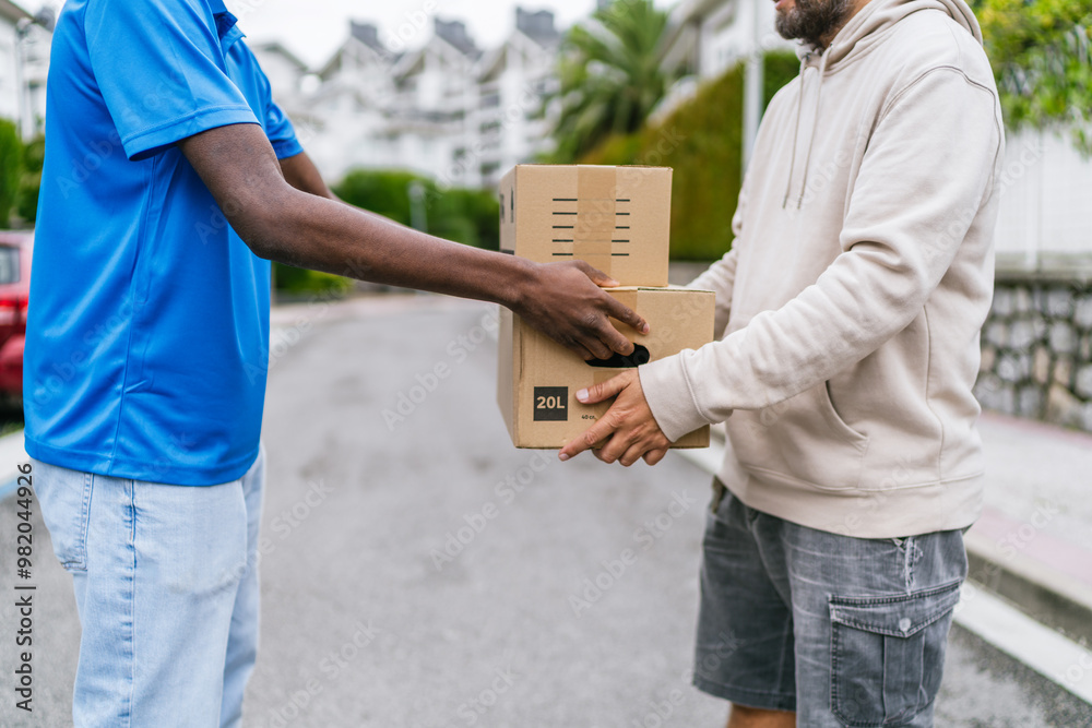 Delivery worker hands a package to a customer in casual clothing on a suburban street. Delivery worker hands a package to a customer in casual clothing on a suburban street.