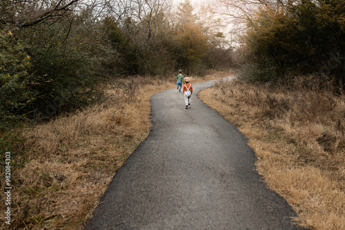 two children running on paved path towards trees under golden light