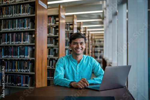Indian student in turquoise kurta with laptop sitting at modern library desk