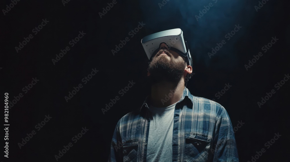 A man wearing a VR headset gazes upward in a dark environment, immersed in virtual reality. A man wearing a VR headset gazes upward in a dark environment, immersed in virtual reality.