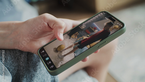 Smartphone application with various video content displayed on phone screen. Close up of teenager scrolling and watching social media feed with short videos using mobile phone while sitting on sofa. photo
