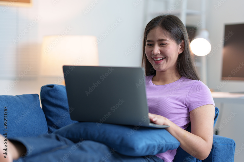 Attractive woman using laptop, mobile phone on sofa in living room relaxing, watching movie, doing research. Learning through the online world Technology and communication concepts. Attractive woman using laptop, mobile phone on sofa in living room relaxing, watching movie, doing research. Learning through the online world Technology and communication concepts.
