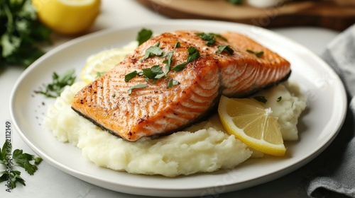 Crispy seared salmon fillet atop a bed of buttery mashed potatoes, elegantly presented on a white plate with fresh herbs and lemon slices.