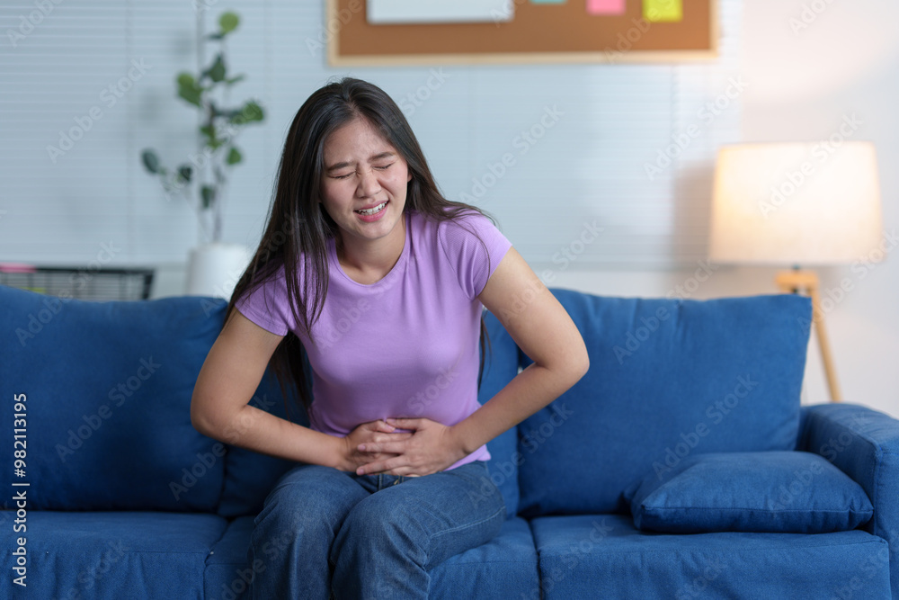 A woman with a sneeze is feeling unwell. Runny nose and sneezing, stomach ache, sore throat, fatigue in the living room on the sofa in the house. Feeling bad and having allergies treatment concept. A woman with a sneeze is feeling unwell. Runny nose and sneezing, stomach ache, sore throat, fatigue in the living room on the sofa in the house. Feeling bad and having allergies treatment concept.