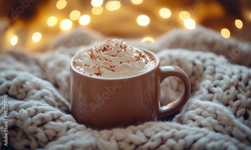 A mug of hot chocolate with whipped cream on top is sitting on a blanket