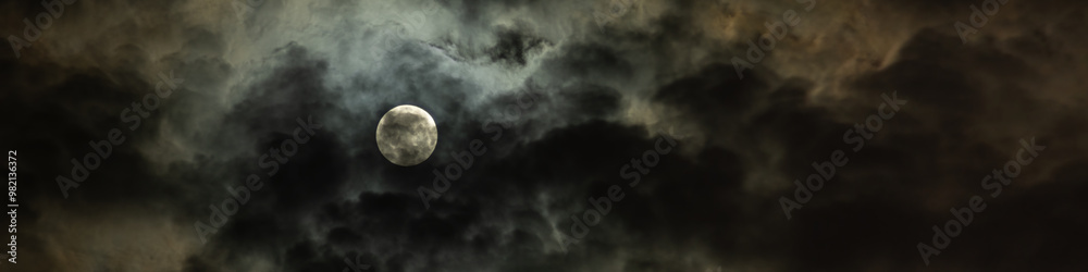 full moon slightly hidden in dramatic night sky with overcast clouds fantasy widescreen panoramic view with large copy space 20:5 format