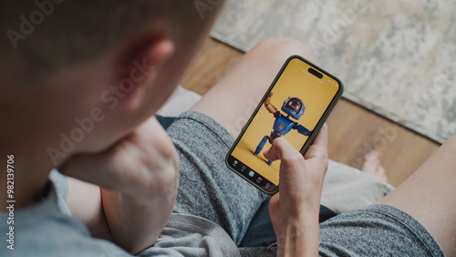 Fotografie Teen boy scrolls through and watches social network feed with short videos using mobile phone while sitting on sofa