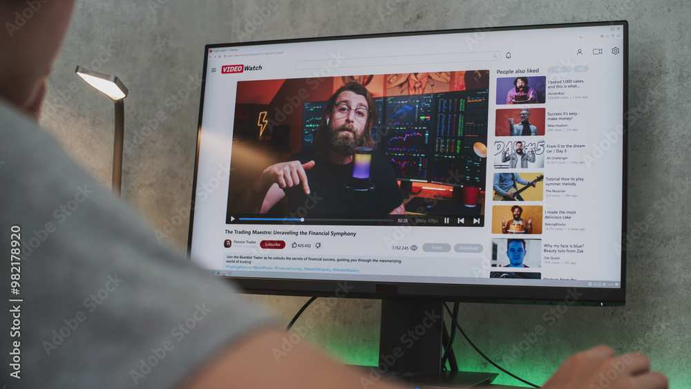 PC monitor shows video sharing platform with blogger content about stock trading. Teen boy in headphones watches educational video about investment and cryptocurrency on personal computer at home. PC monitor shows video sharing platform with blogger content about stock trading. Teen boy in headphones watches educational video about investment and cryptocurrency on personal computer at home.