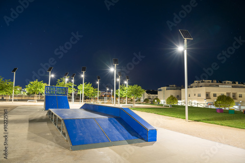 Skate park with ramps and rails in a clean urban environment, illuminated at night by several solar-powered street lights, highlighting the sustainable energy infrastructure in public spaces. Spain