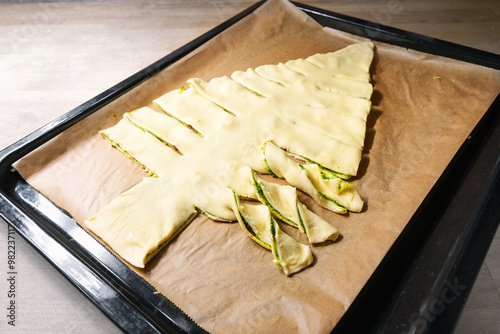 Puff pastry dough filled with homemade green pesto is cut in a Christmas tree on a baking tray, creative recipe for a holiday party, copy space, selected focus