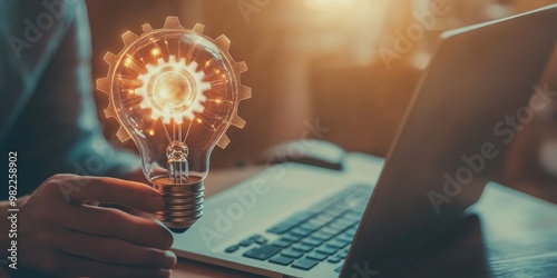 A light bulb with a gear icon symbolizes innovation and technological creativity, with a man using a notebook computer to develop new ideas and inspire innovation.