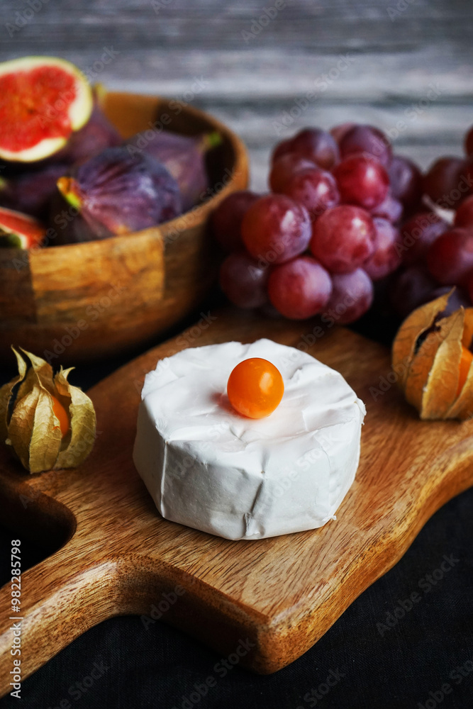 Ripe figs next to Brie cheese on a wooden board, pink grapes and Physalis fruits on a dark background Ripe figs next to Brie cheese on a wooden board, pink grapes and Physalis fruits on a dark background