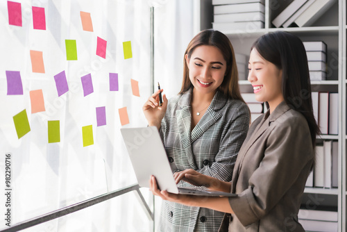 Two businesswoman reading business data on laptop and writing strategy ideas in sticky notes