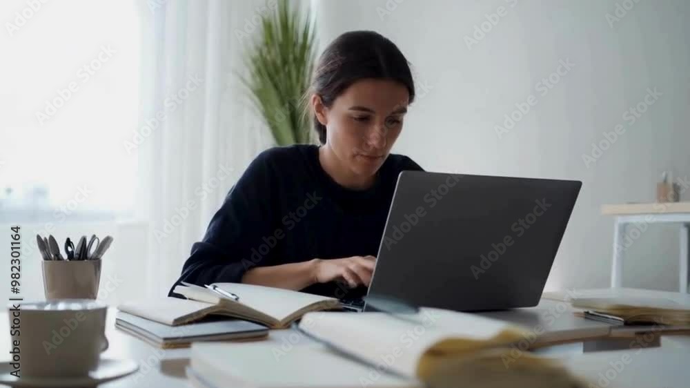 Woman Working on Laptop at a Desk with Open Notebooks Woman Working on Laptop at a Desk with Open Notebooks