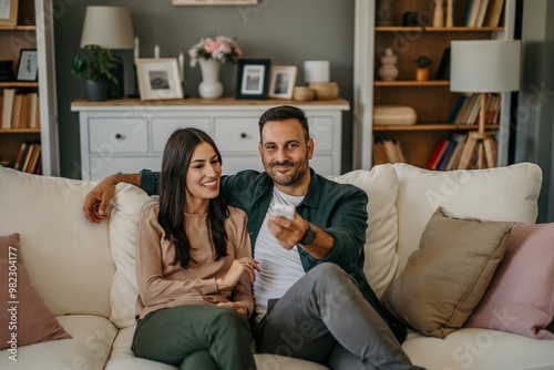 Embraced diverse couple watching television while relaxing together on their living room sofa at home