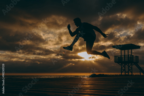 Full body sideways young strong sporty athletic toned fit sportsman man wear sports clothes jump high warm up training at sunrise sun dawn over sea beach outdoor on pier seaside in summer day morning.