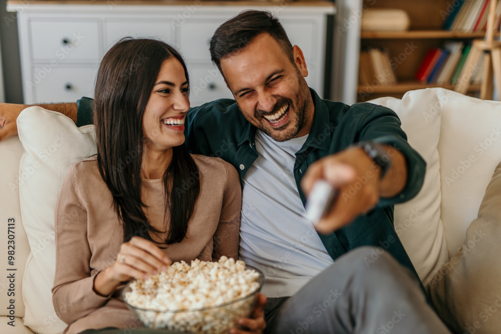 Shot of a beautiful happy couple sitting on the sofa in the living room at home, laughing and watching TV. Shot of a beautiful happy couple sitting on the sofa in the living room at home, laughing and watching TV.