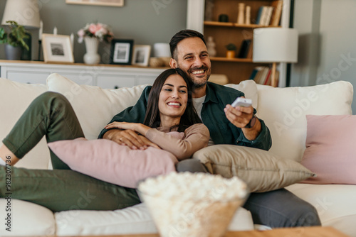 Fotografie Diverse couple, watching tv and remote on living room couch with smile, hug or r