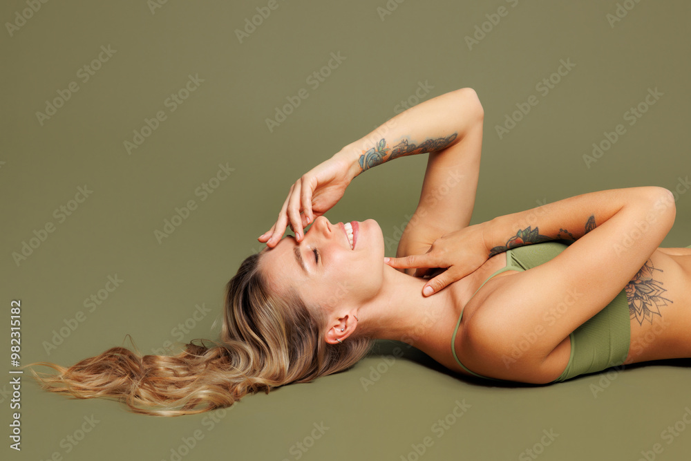 Fototapeta premium Side profile view young smiling fun nice lady woman with slim skinny body perfect skin wear top bra lingerie lay don on floor touch nose isolated on plain green background. Lifestyle diet fit concept.