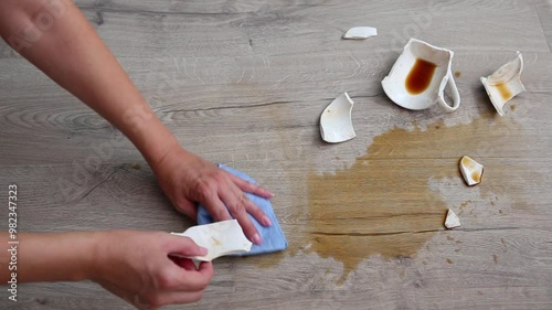 A broken cup of coffee fell on laminate, coffee spilled on floor.