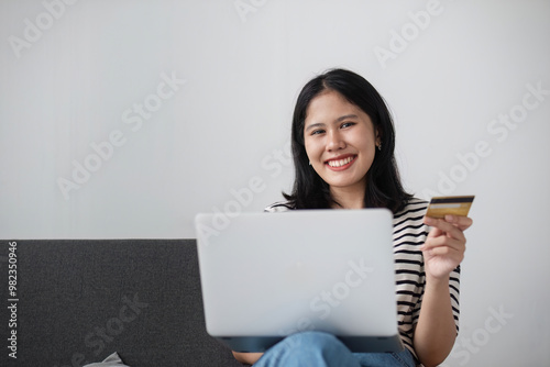 Young Woman Smiling While Shopping Online and Paying with Credit Card on Laptop at Home