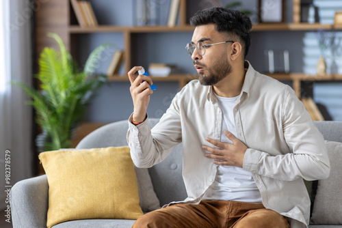 Fotografie Man using inhaler while experiencing respiratory discomfort on sofa at home