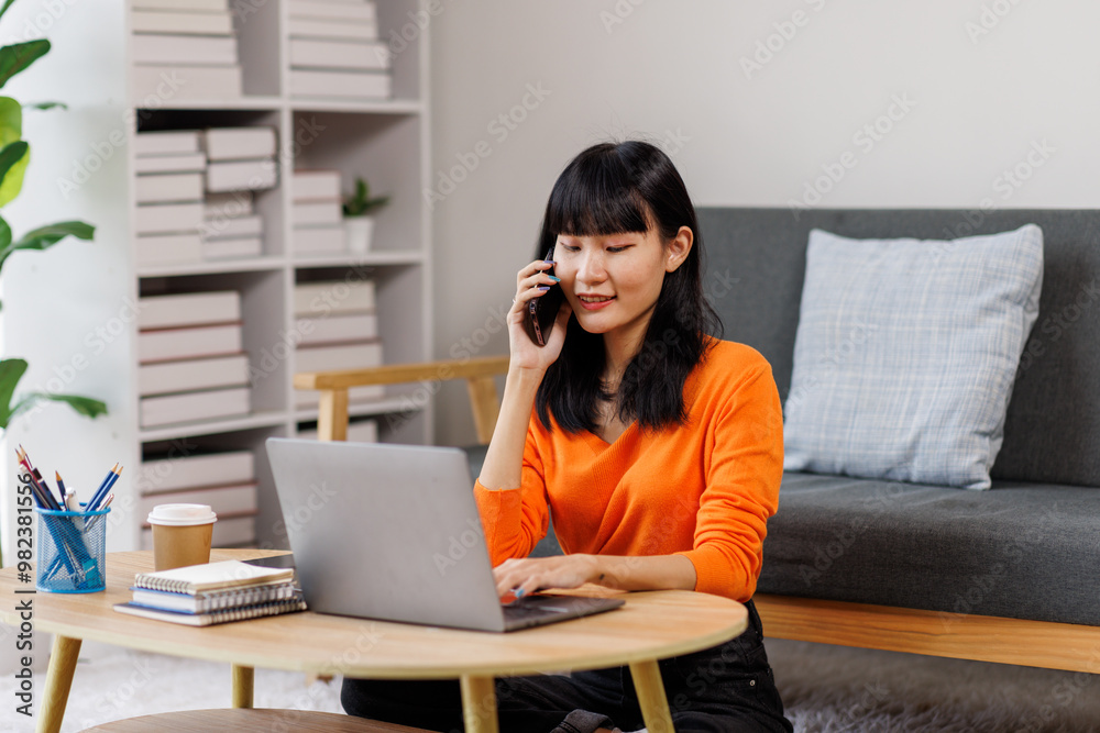 Portrait of a smiling young woman working at home with laptop and talking on mobile phone
