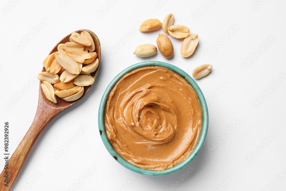 Tasty peanut butter in bowl and spoon with groundnuts on white table, flat lay Tasty peanut butter in bowl and spoon with groundnuts on white table, flat lay