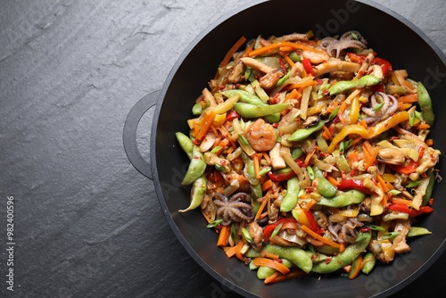 Stir-fry sea food in wok on grey textured table, top view. Space for text