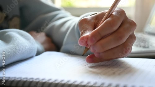 Detalhe de mão de estudante escrevendo no caderno na bancada de estudos. 