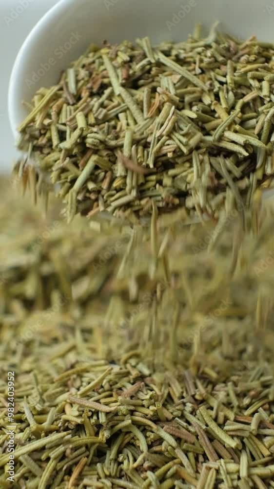Seasoning dried chopped rosemary pouring out of spoon, vertical slow motion Seasoning dried chopped rosemary pouring out of spoon, vertical slow motion
