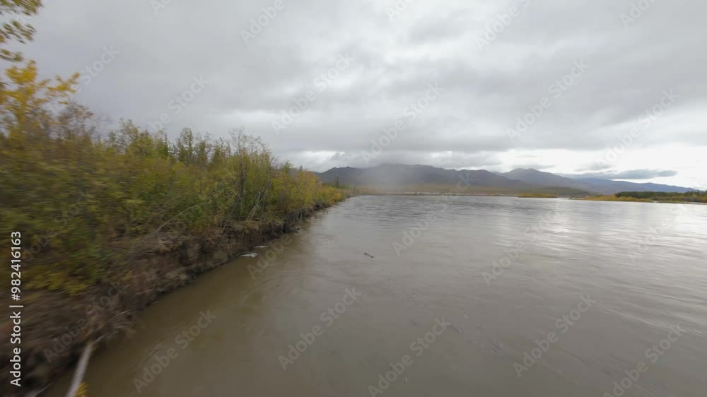 Experience the serene beauty of a quiet riverbank adorned with autumn foliage. The drone glides smoothly over the water, revealing the lush trees and distant mountains.