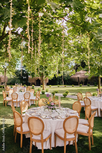 Obraz na płótnie Outdoor Wedding Reception with Brown Chairs and Decorated Tables on a Green Lawn in a Scenic Nature Setting w salonie