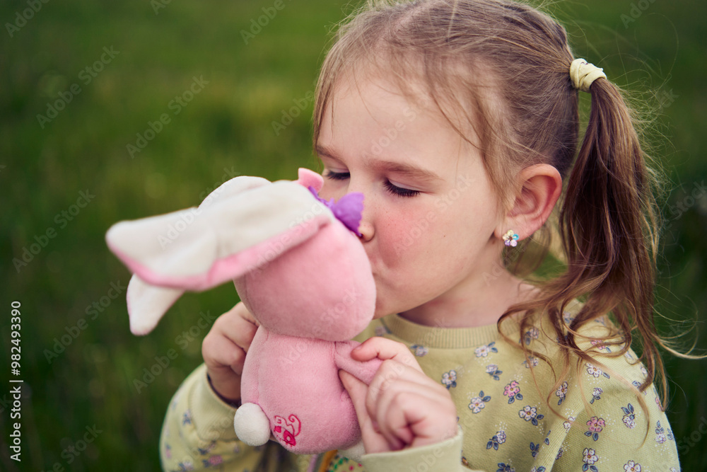 a beautiful blond girl with her toy bunny is playing in the field