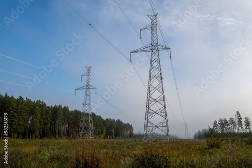 Electric transmission lines in the foggy morning autumn forest. Power lines.